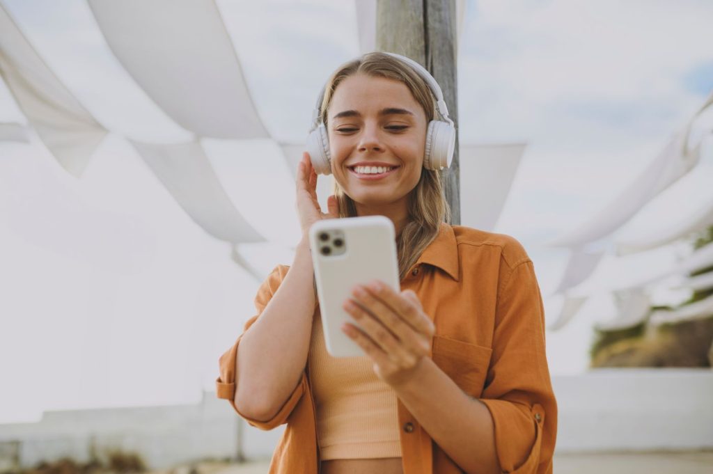 Mulher loira sorrindo e ouvindo música pelo seu Tiktok no celular