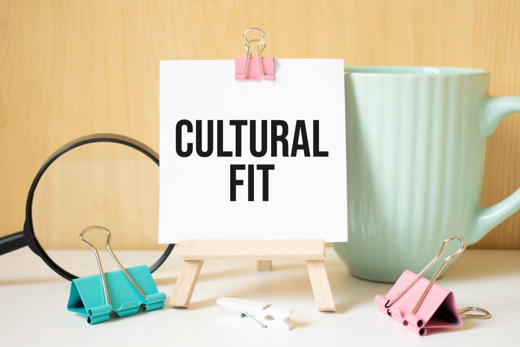 Texto "CULTURAL FIT" escrito em caderno preto com lupa e uma caneta. Conceito de negócios e realização.