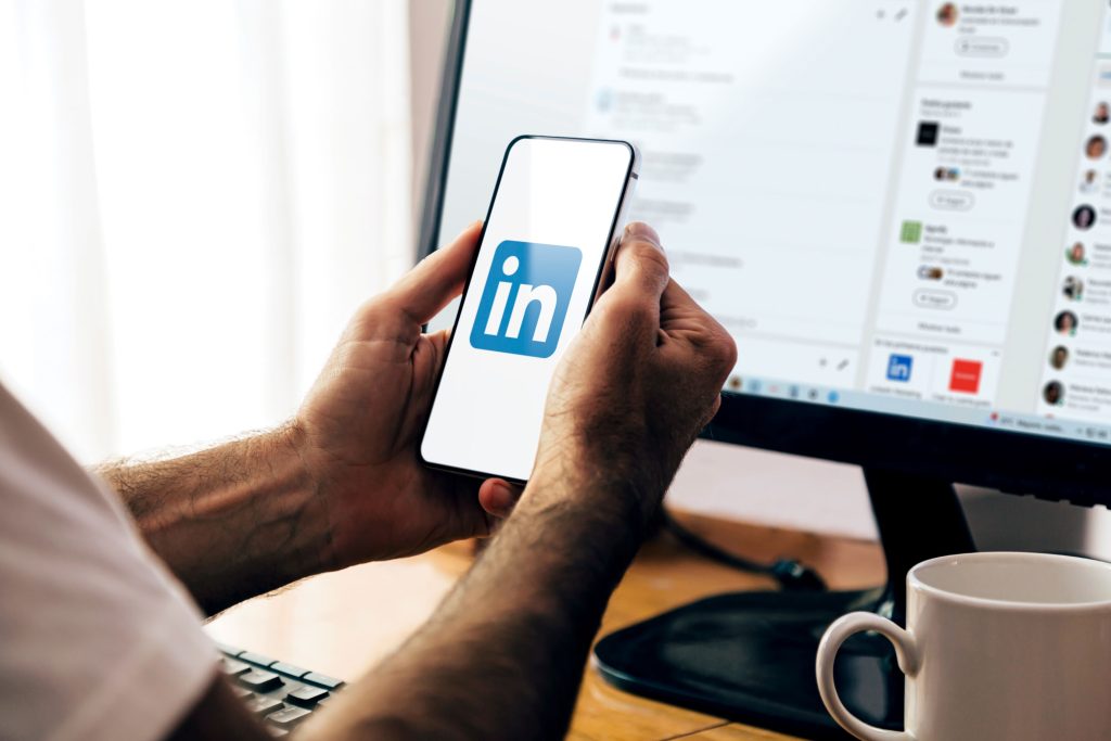 Homem com celular na mão e a imagem com letras in logotipo do linkedin