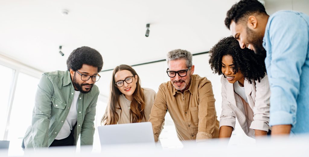 Uma equipe diversa de colegas se envolve com entusiasmo com o conteúdo em um laptop, retratando uma cultura de trabalho colaborativa e uma sessão eficaz de brainstorming em um escritório contemporâneo.