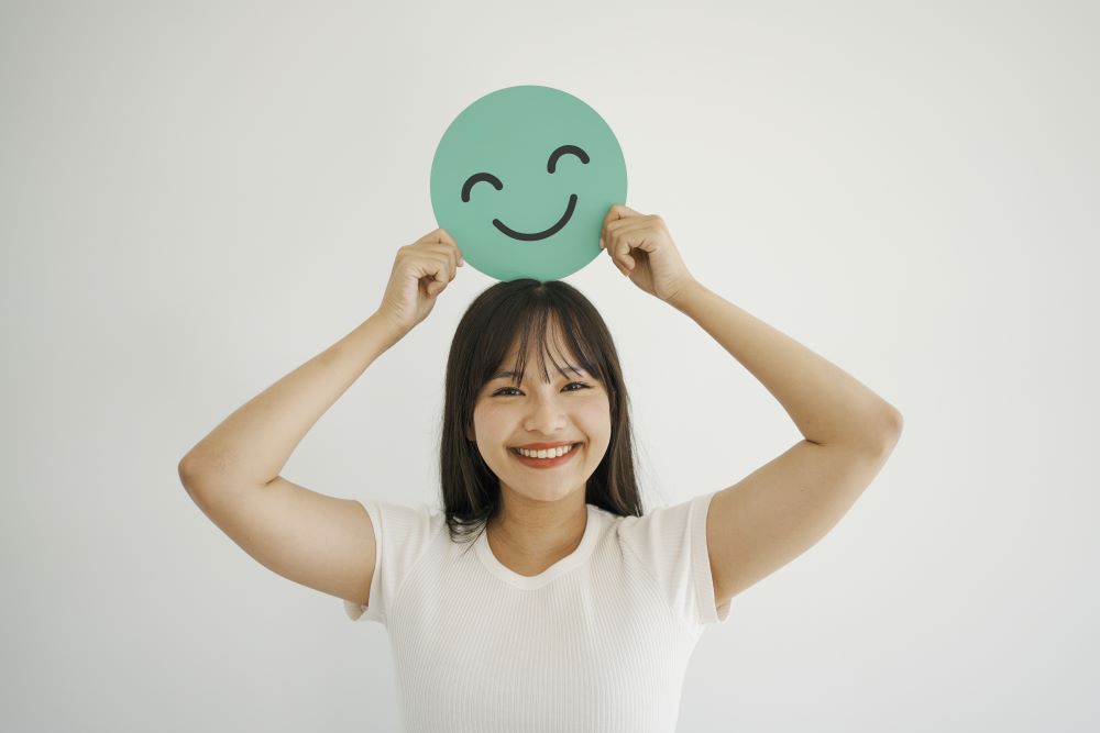 Jovem asiática feliz segurando um emoji de sorriso, conceito de saúde mental positiva, Dia Mundial da Saúde Mental.