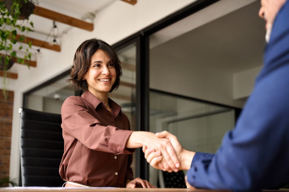 Feliz jovem empresária gerente de banco apertando as mãos da cliente na reunião. Mulher sorridente que contrata recrutas na entrevista de emprego, agente de seguros, advogado que faz acordo de contrato no trabalho com o aperto de mão do negócio.